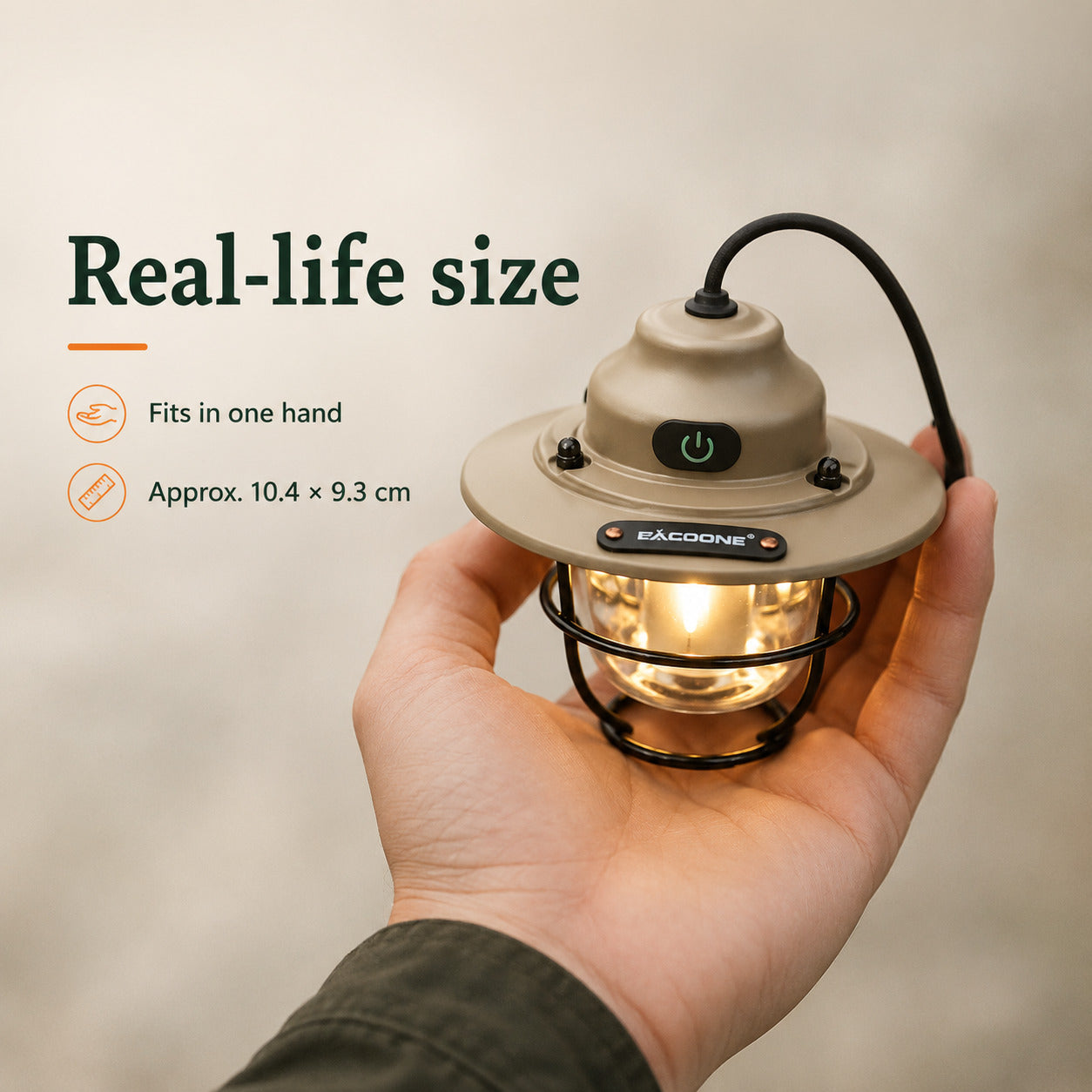 A hand holds a small camping lantern with a warm glowing light inside. The lantern has a beige top and bottom with a black wire cage and power button.